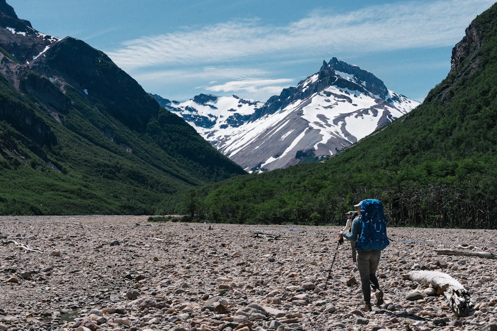 a person with a backpack walking on a rocky area with mountains in the background