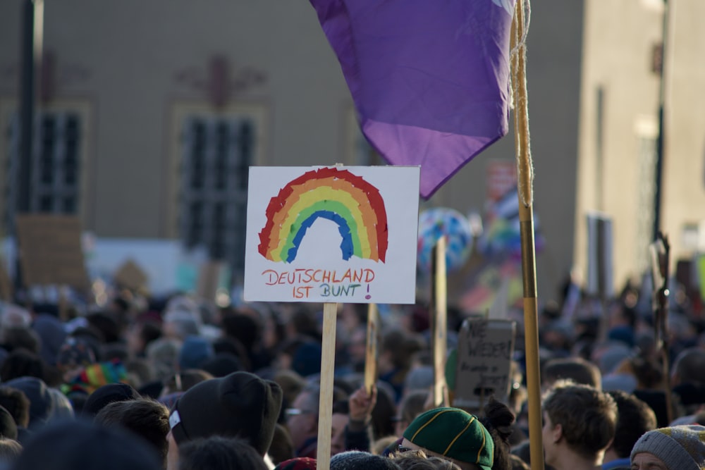 una folla di persone con un cartello e una bandiera arcobaleno