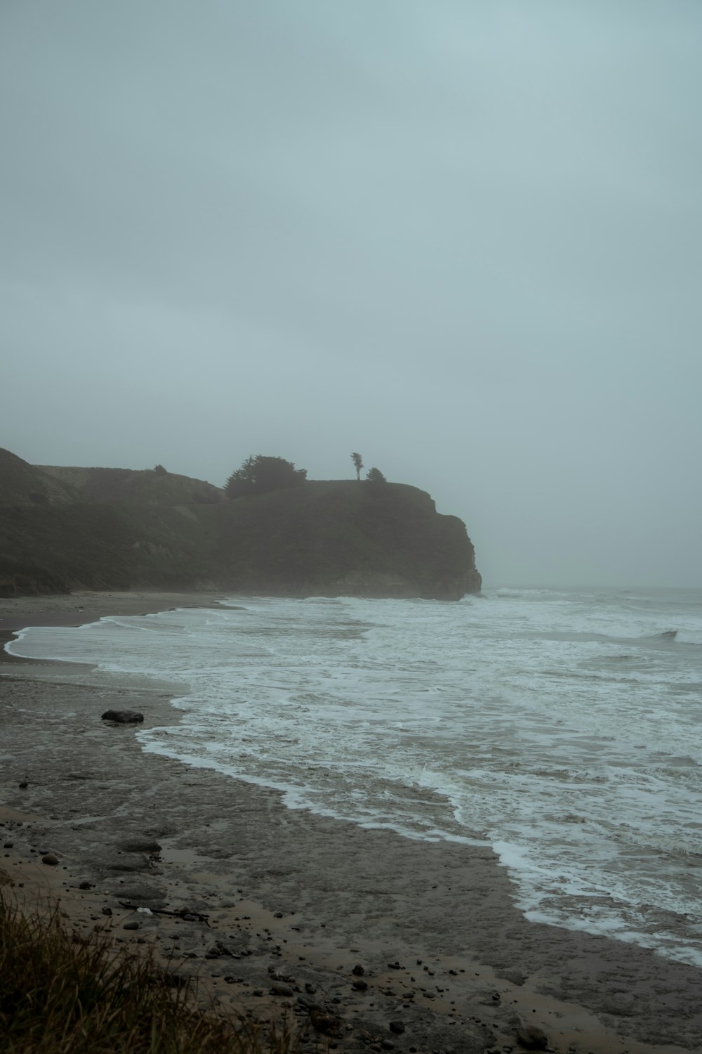 a foggy day at the beach with a lighthouse on a hill in the distance