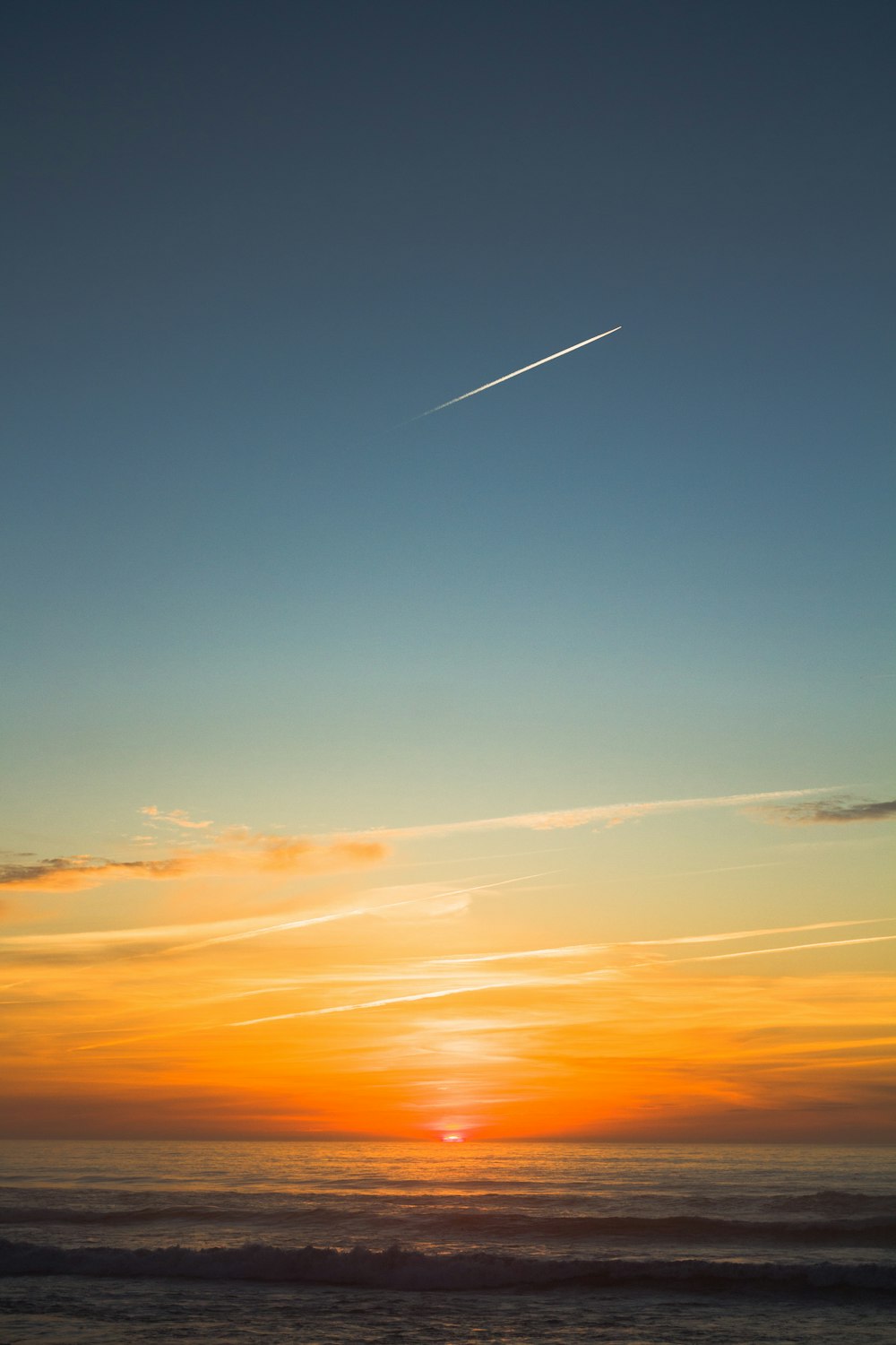 a plane flying over the ocean at sunset