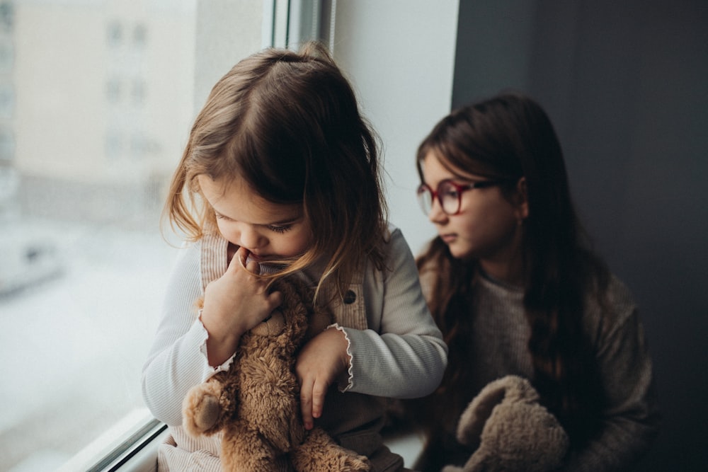 two young girls sitting next to each other on a window sill