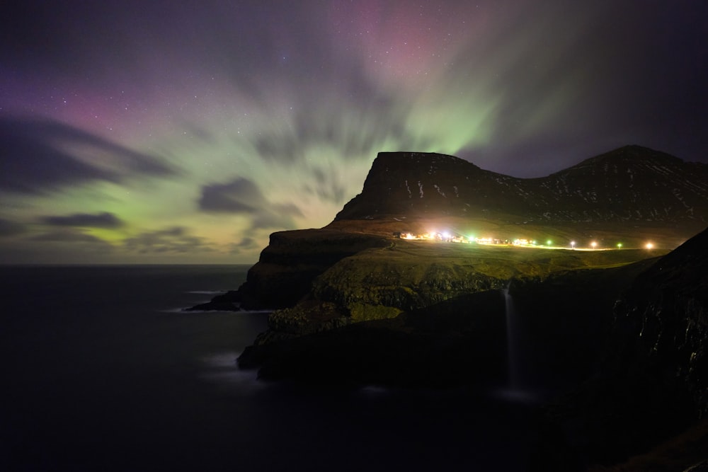 As luzes da aurora brilham intensamente sobre uma montanha e um corpo de água