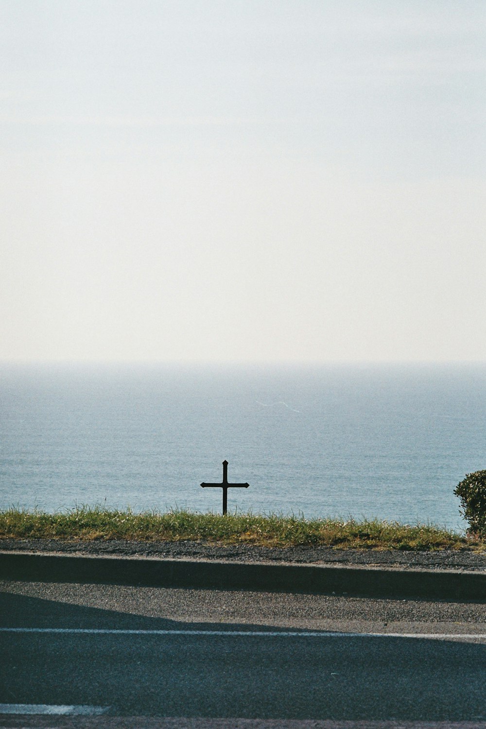 a cross on the side of a road next to the ocean
