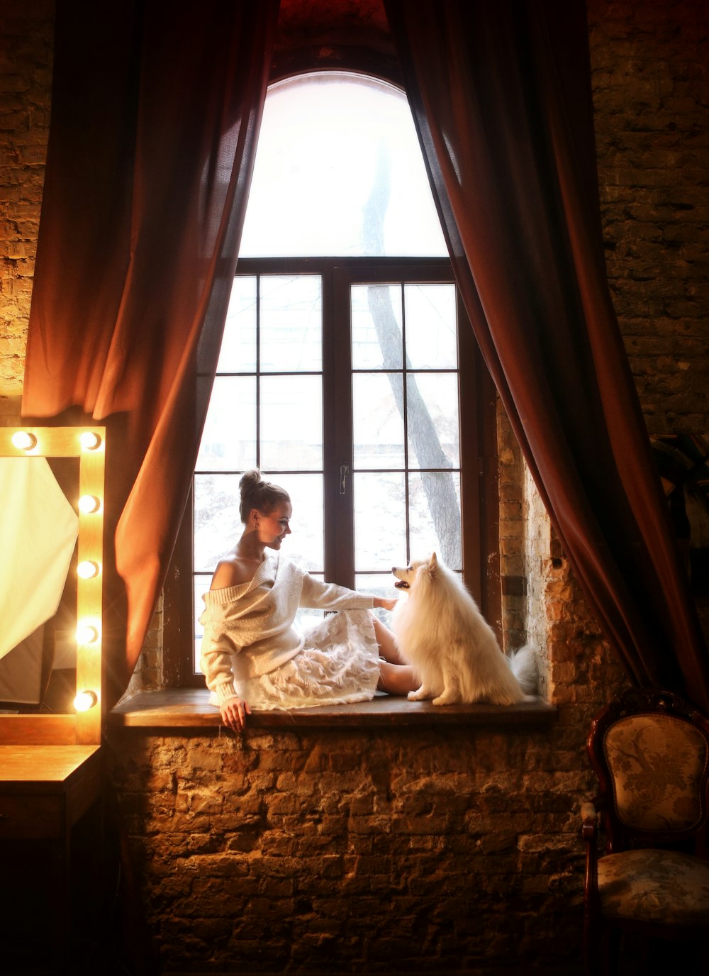 a woman sitting on a window sill next to a dog