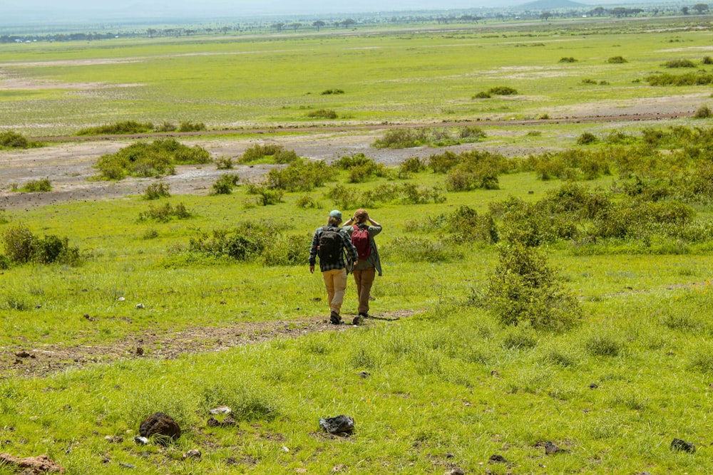 a couple of people walking across a lush green field