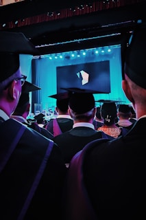 a group of people in graduation gowns watching a screen