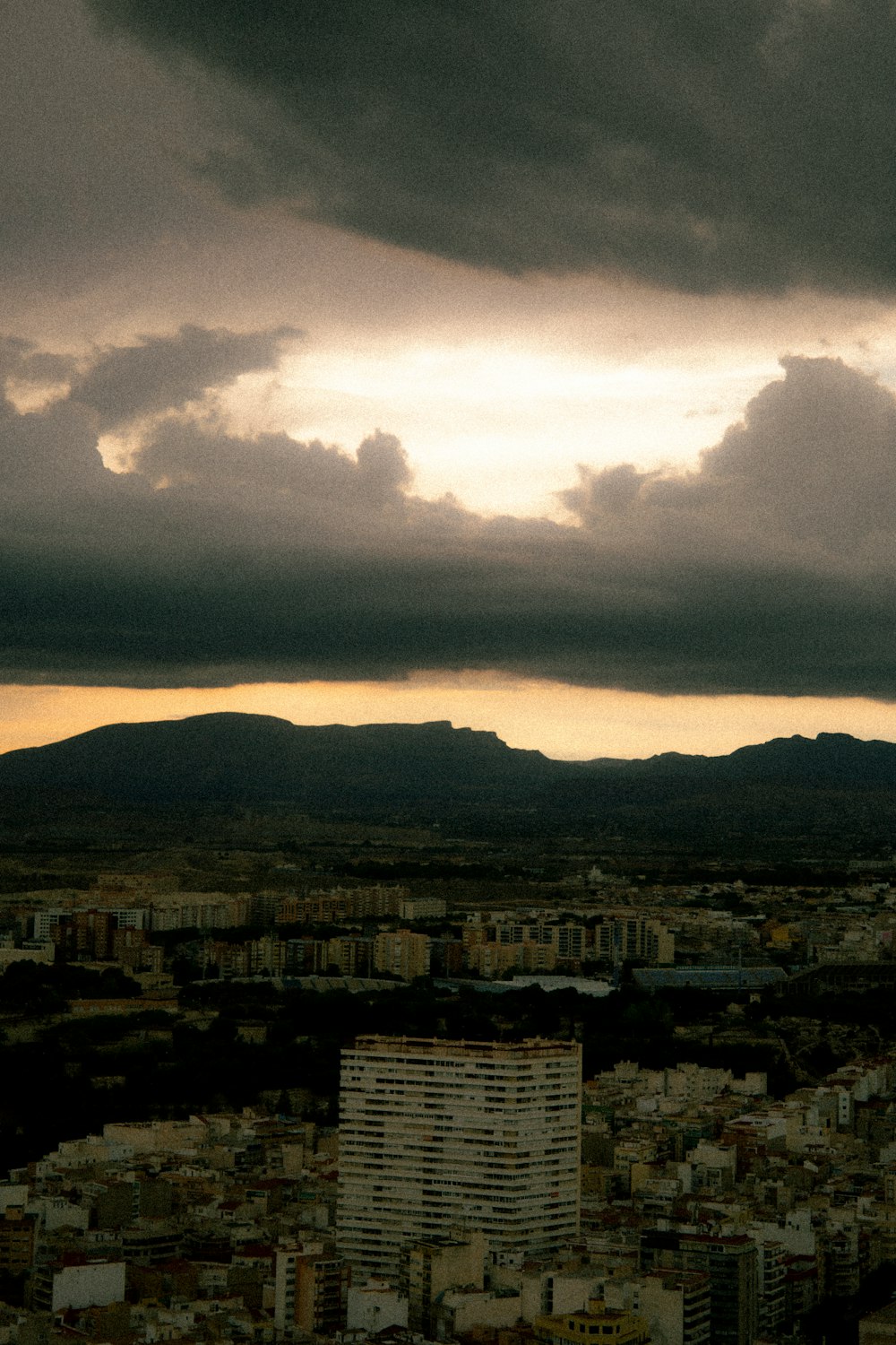 a cloudy sky over a city with mountains in the background