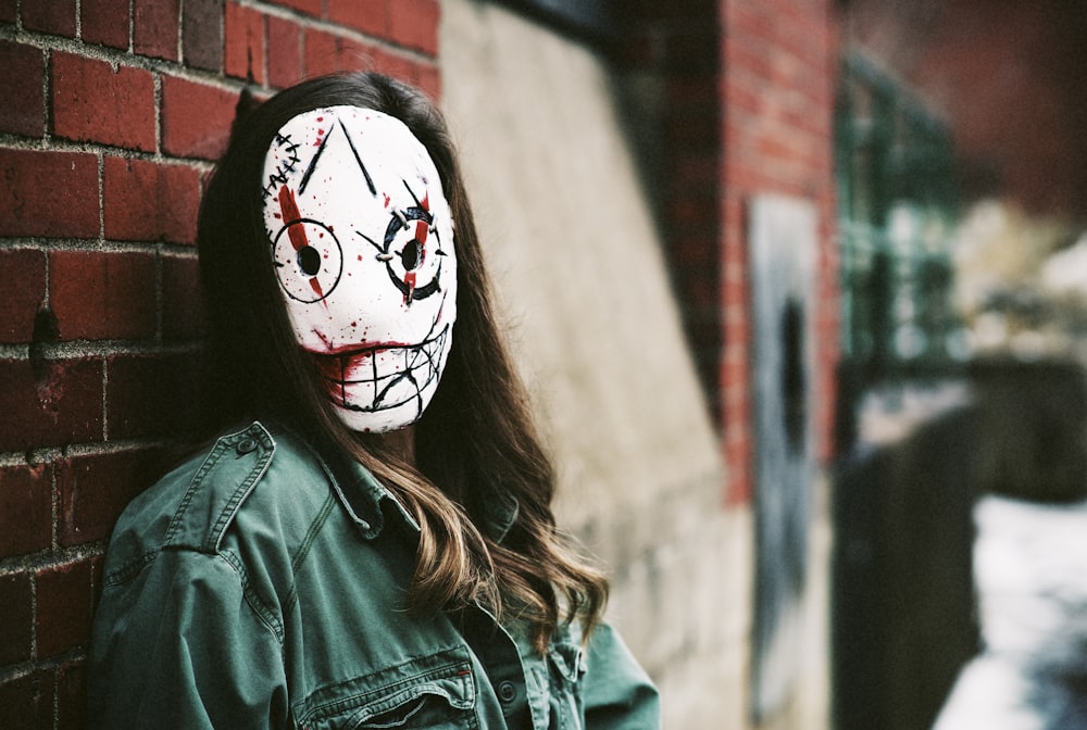 a woman wearing a white mask standing next to a brick wall