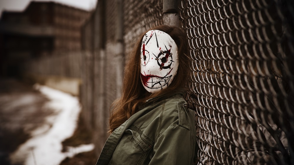a woman wearing a creepy mask leaning against a fence