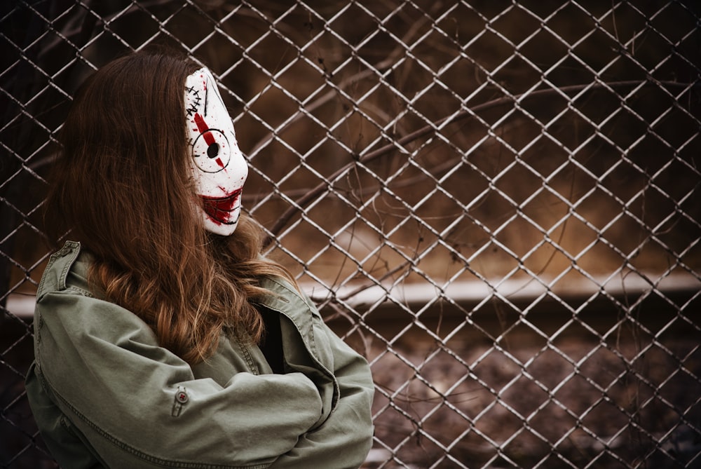 a woman wearing a scary mask behind a chain link fence