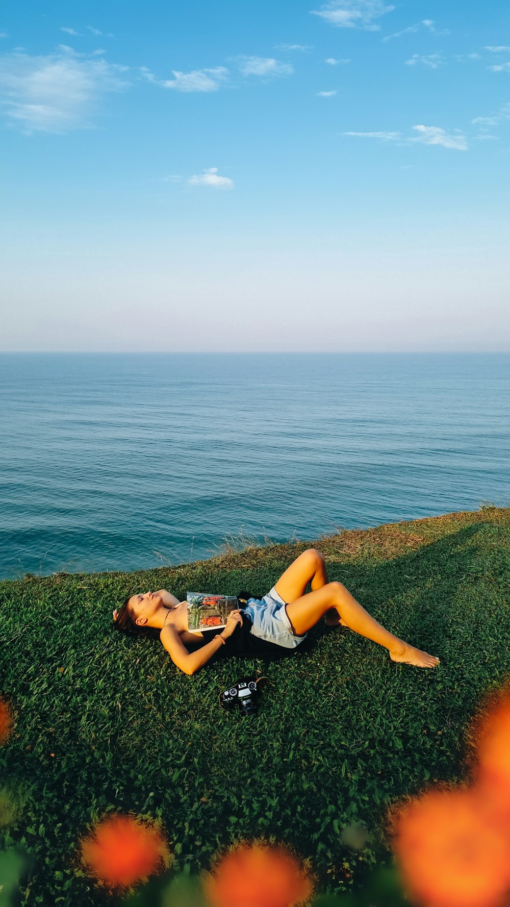 a woman laying on top of a lush green field next to the ocean