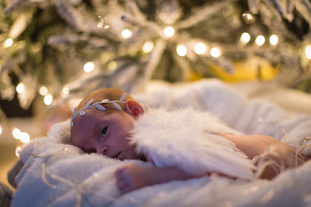 a baby is laying on a blanket in front of a christmas tree
