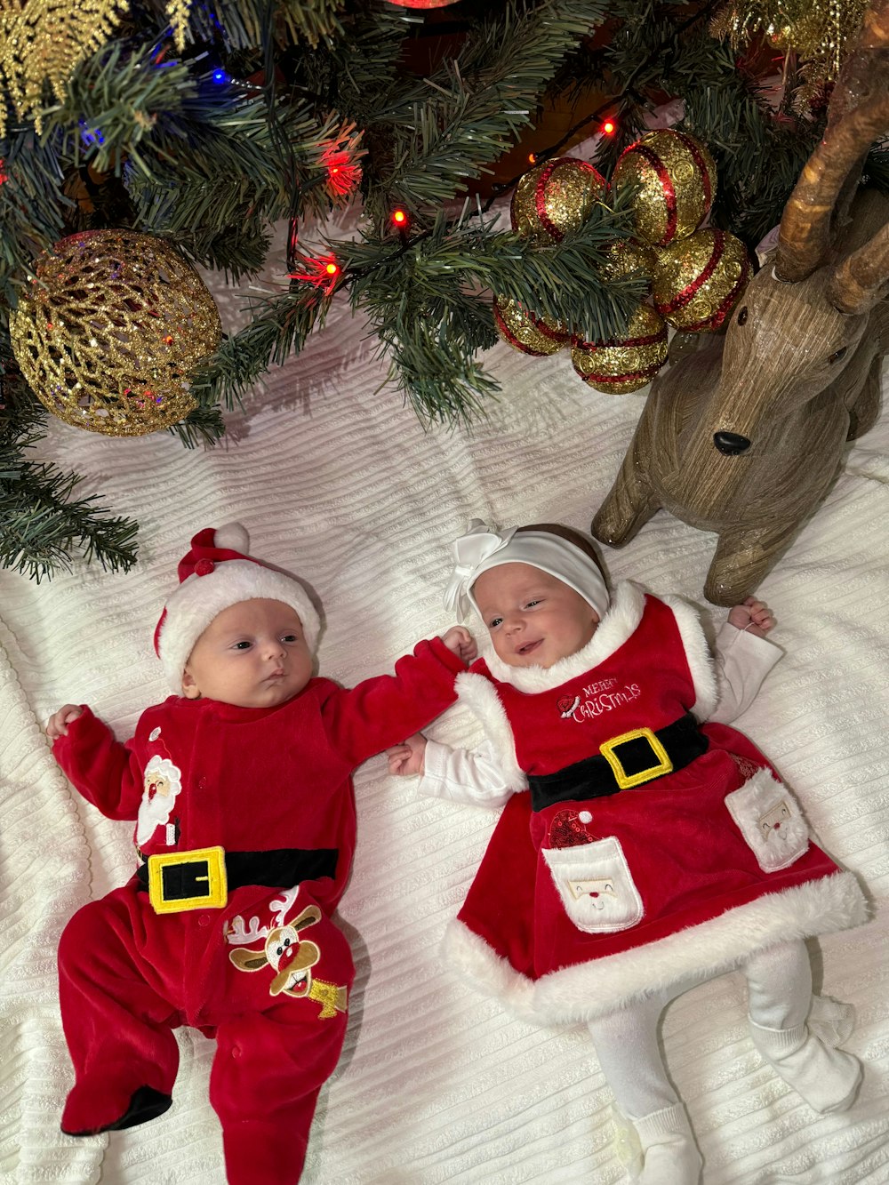 two babies dressed as santa clause laying next to a christmas tree
