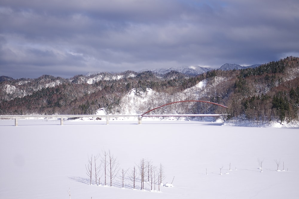 a bridge over a snow covered field with mountains in the background