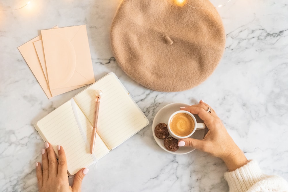 a person is holding a cup of coffee and writing on a notebook