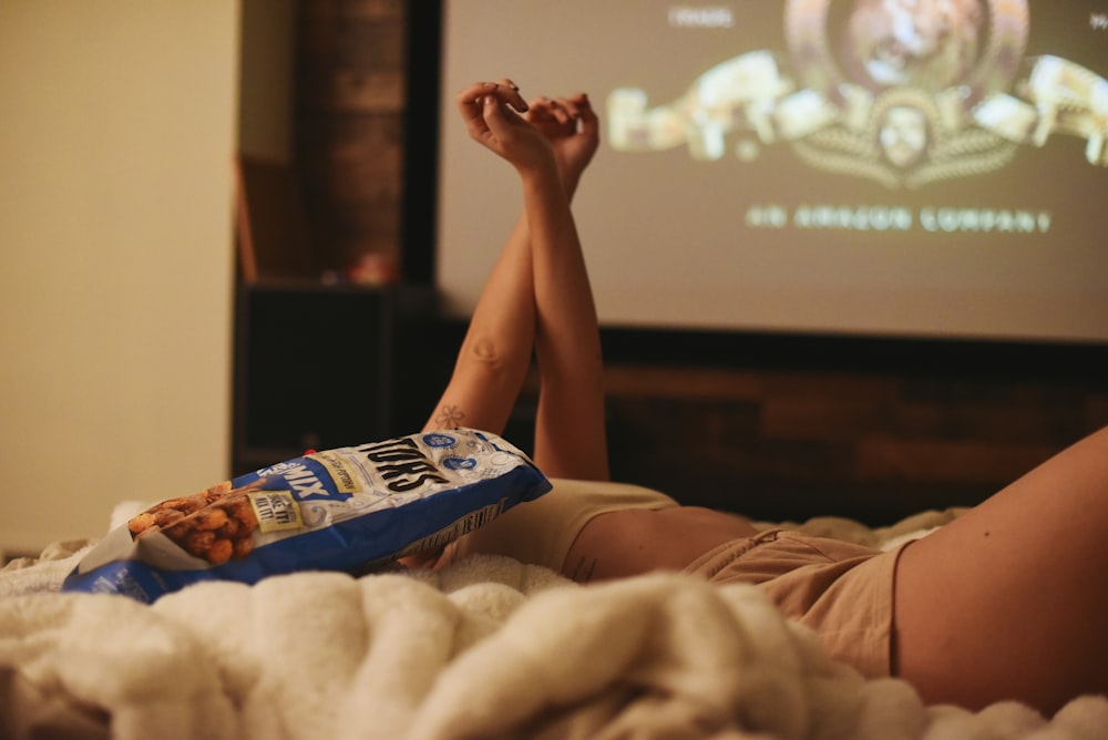 a person laying on a bed with a bag of popcorn