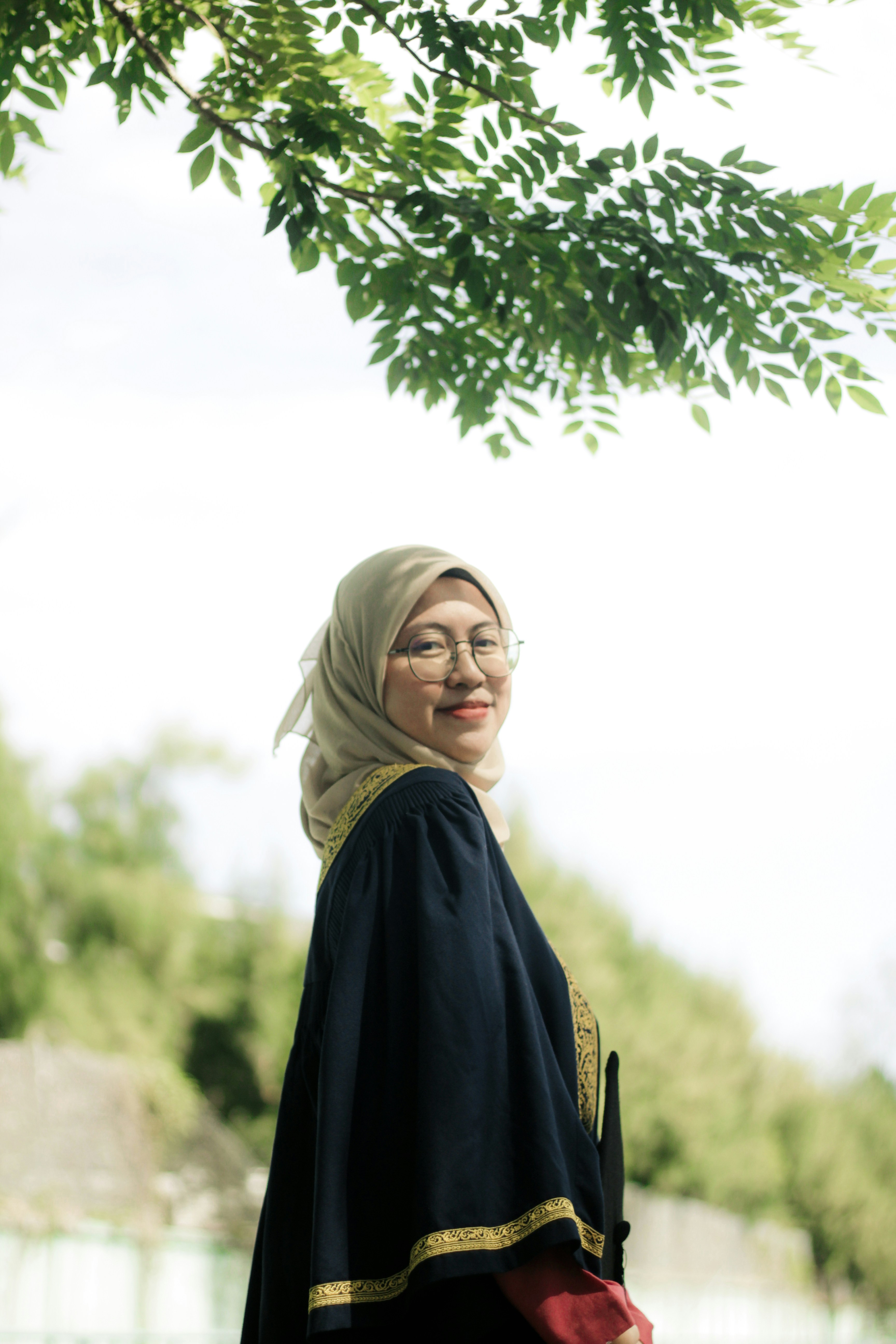 a woman standing under a tree wearing a headscarf