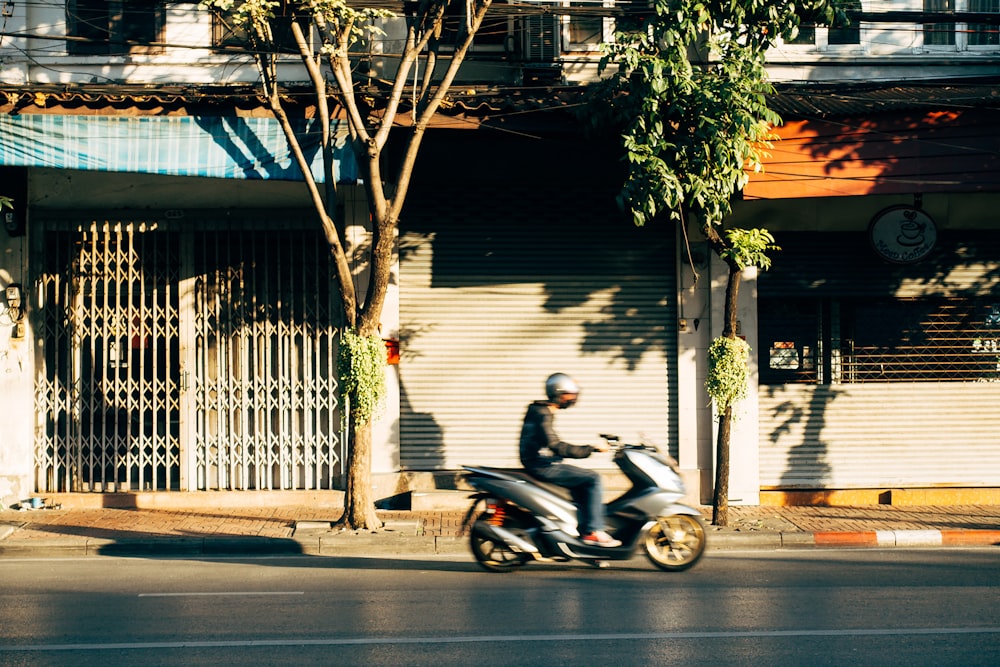 a man riding a scooter down a street next to a tall building