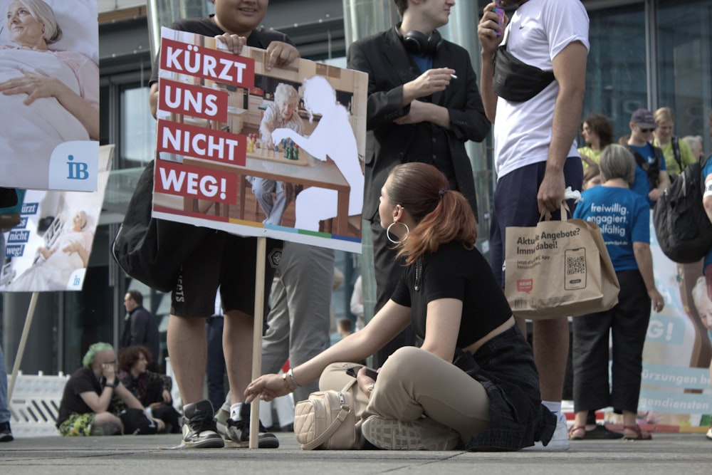 a woman sitting on the ground next to a sign