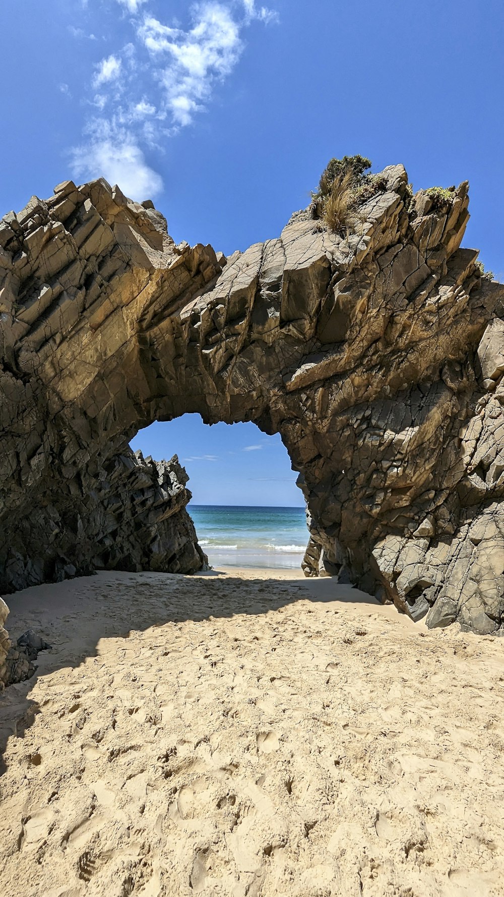 a sandy beach with a rock arch and ocean in the background