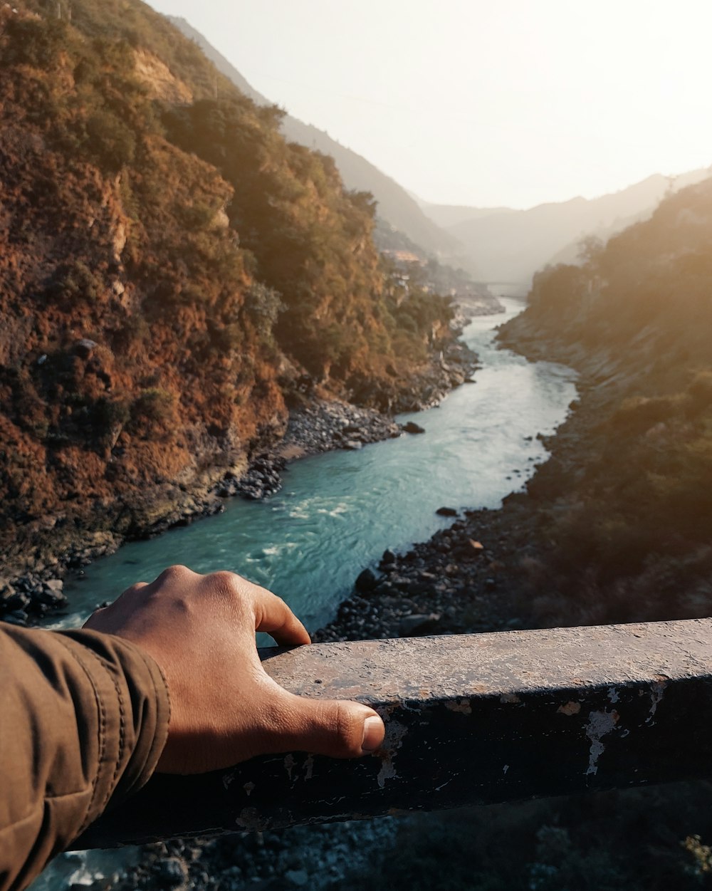 a person's hand on a railing overlooking a river