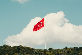 a red flag flying in the wind on top of a hill