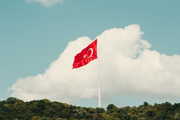 a red flag flying in the wind on top of a hill