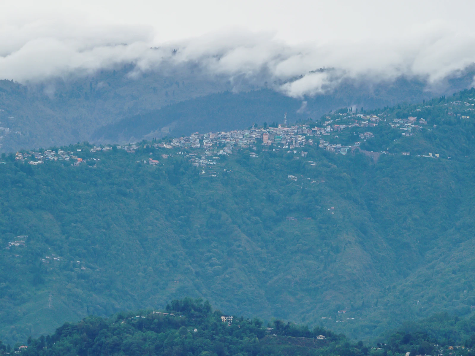 Kalimpong town spread along its green ridge in West Bengal, cloud lying low over the hills behind it