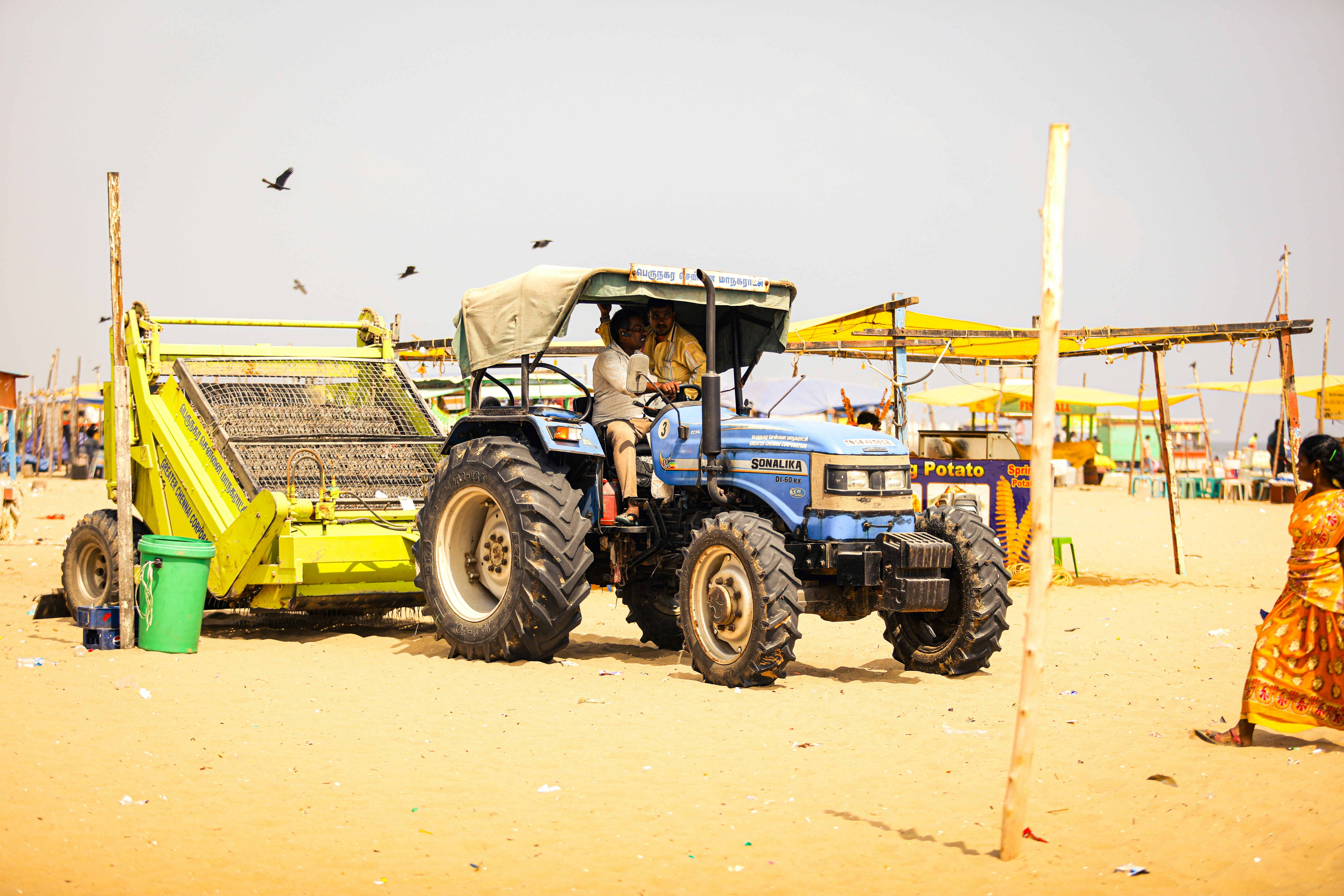 A tractor is parked on the beach with a woman standing next to it