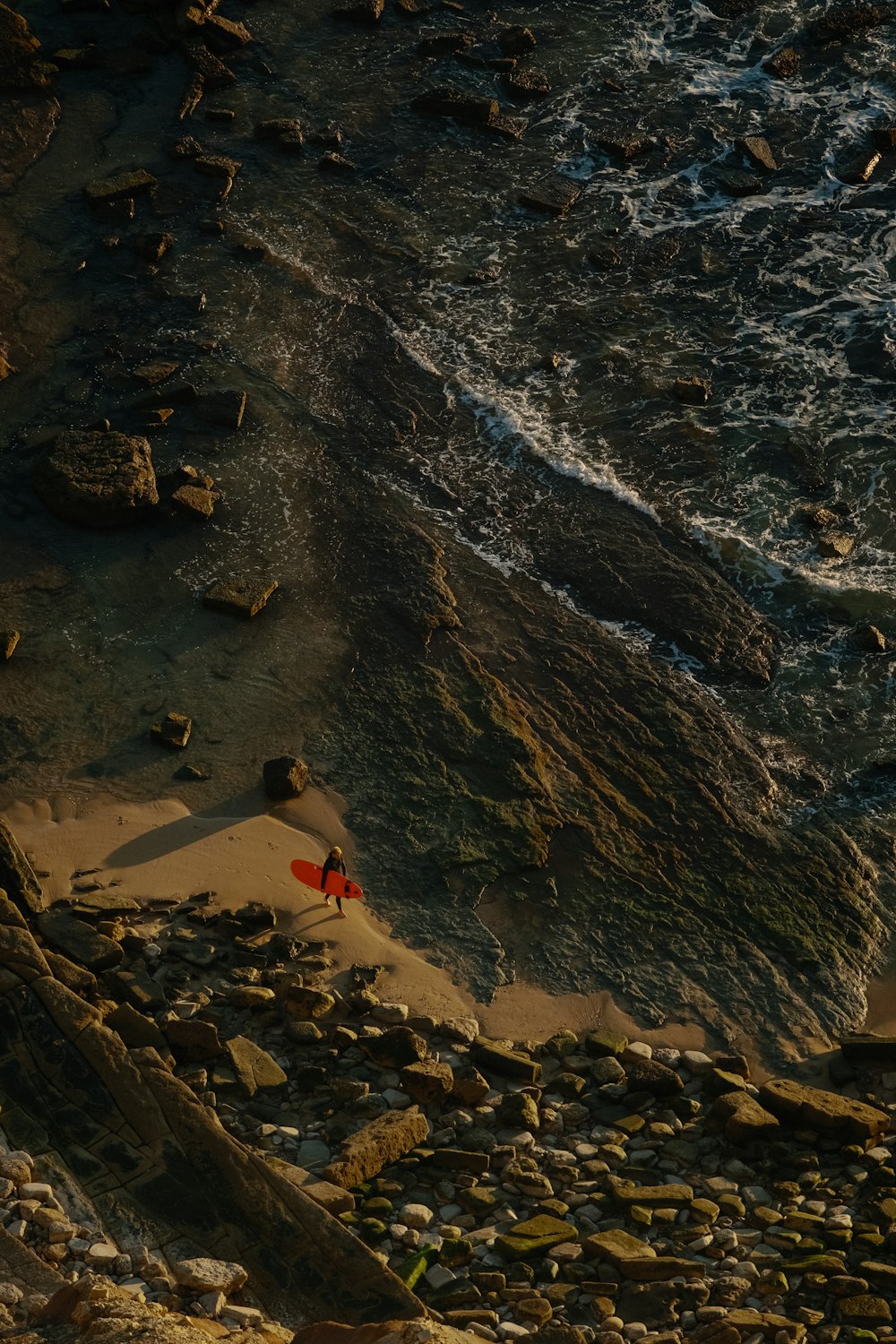 a red surfboard sitting on top of a rocky beach