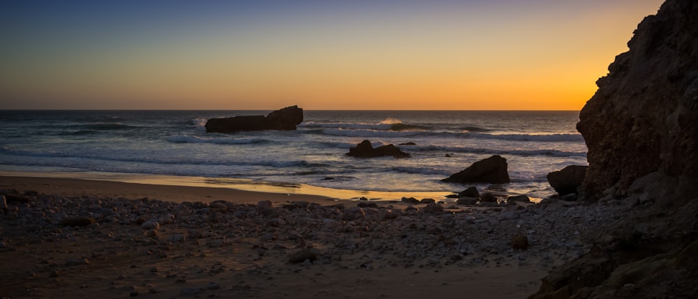 the sun is setting over the ocean and rocks