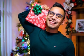 a man holding a wrapped present in front of a christmas tree