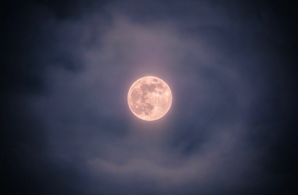 une pleine lune vue à travers un ciel nuageux