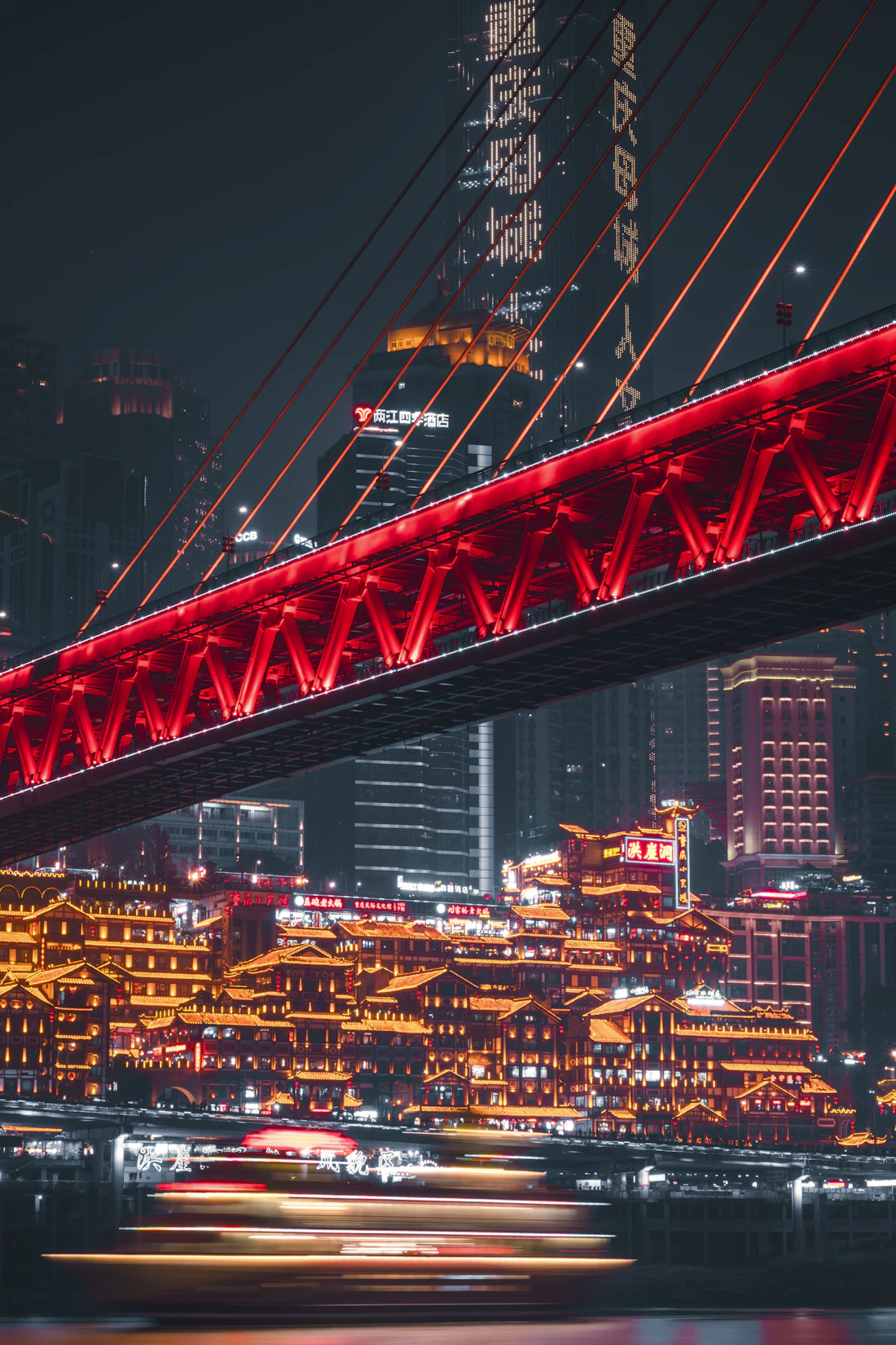 The golden lights of Hongyadong glowing at night beneath a red bridge in Chongqing