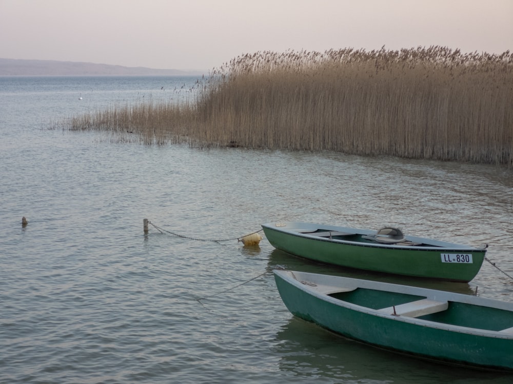 a couple of green boats floating on top of a lake