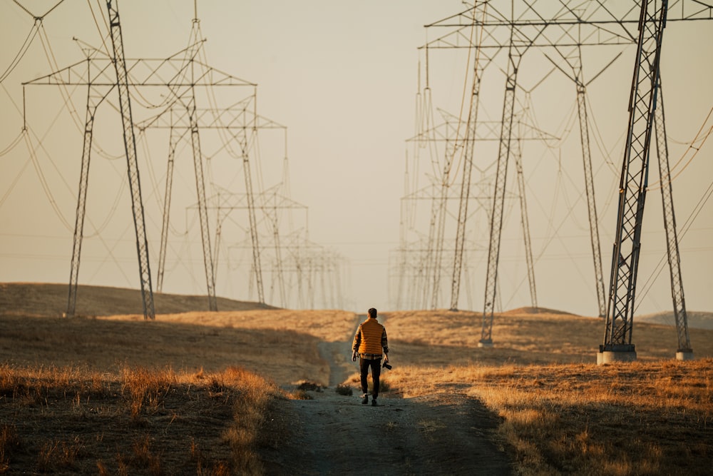 um homem caminhando por uma estrada de terra ao lado de linhas de energia