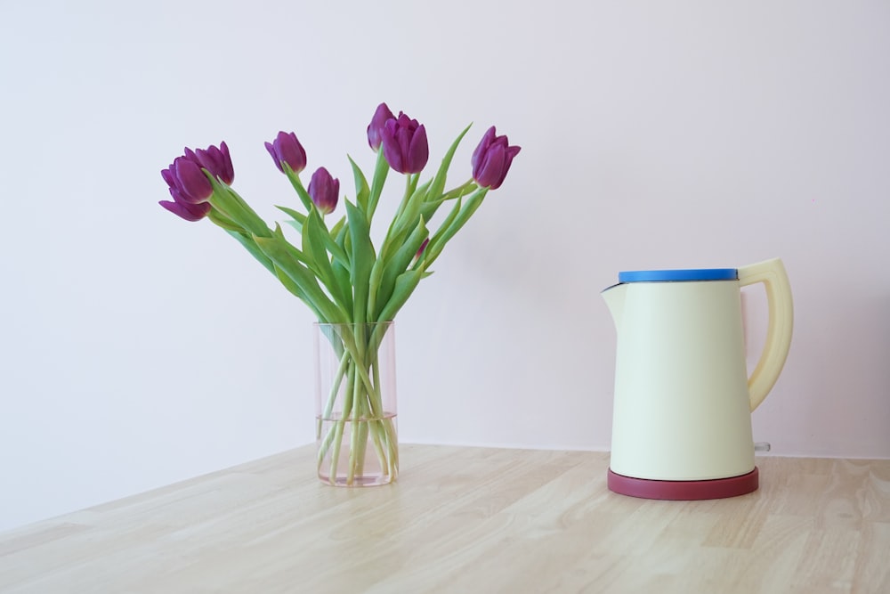 a vase of purple tulips next to a jug of water