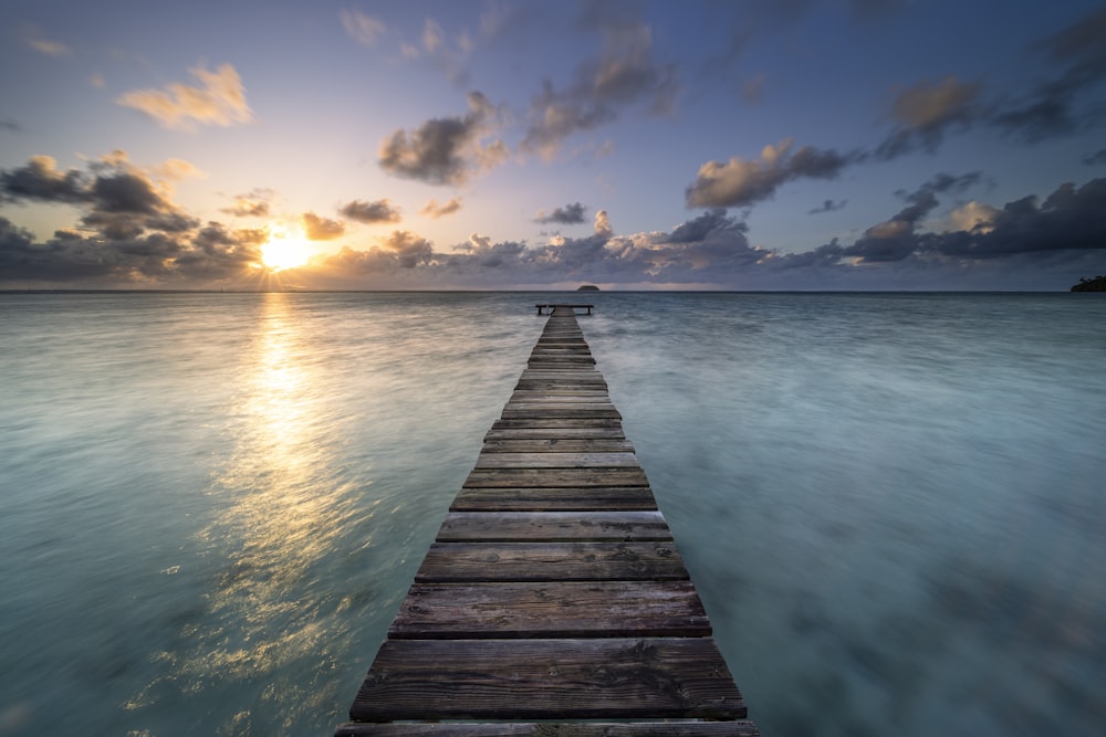 a wooden pier extending into the ocean at sunset