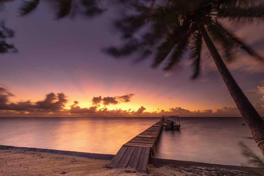 the sun is setting over the ocean with a dock