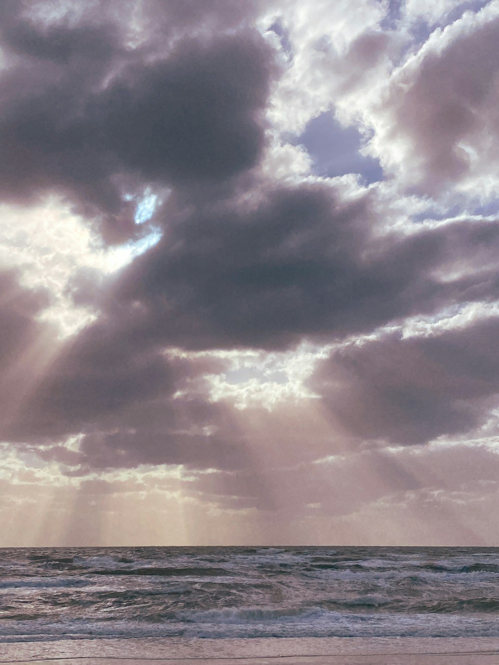 a person walking on a beach with a surfboard under a cloudy sky