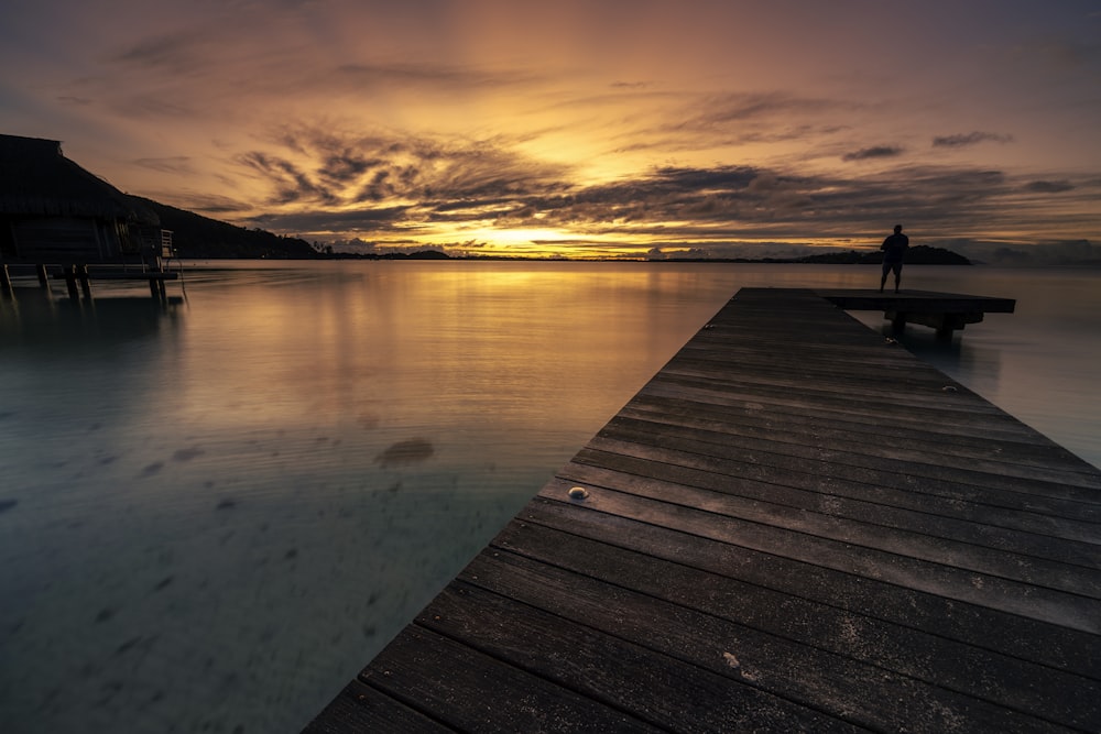 a person standing on a dock at sunset
