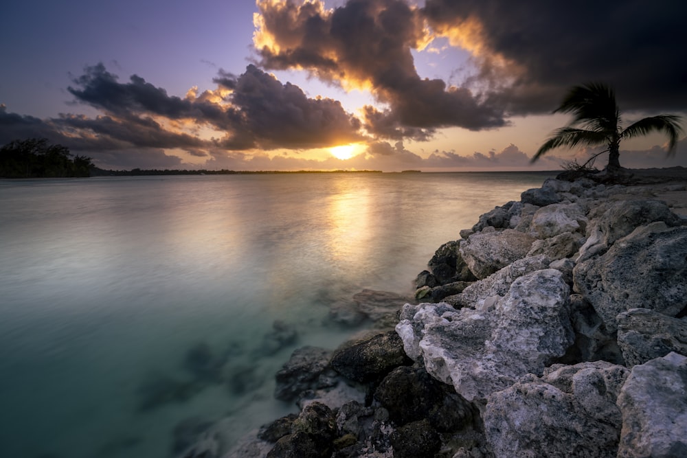 the sun is setting over the ocean with rocks