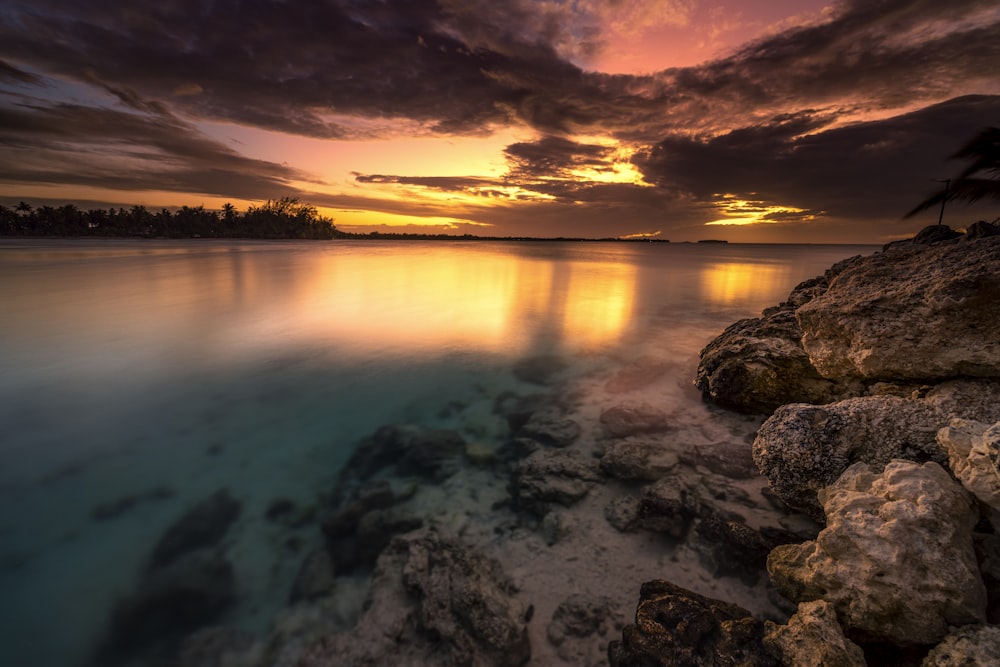 a beautiful sunset over the ocean with rocks