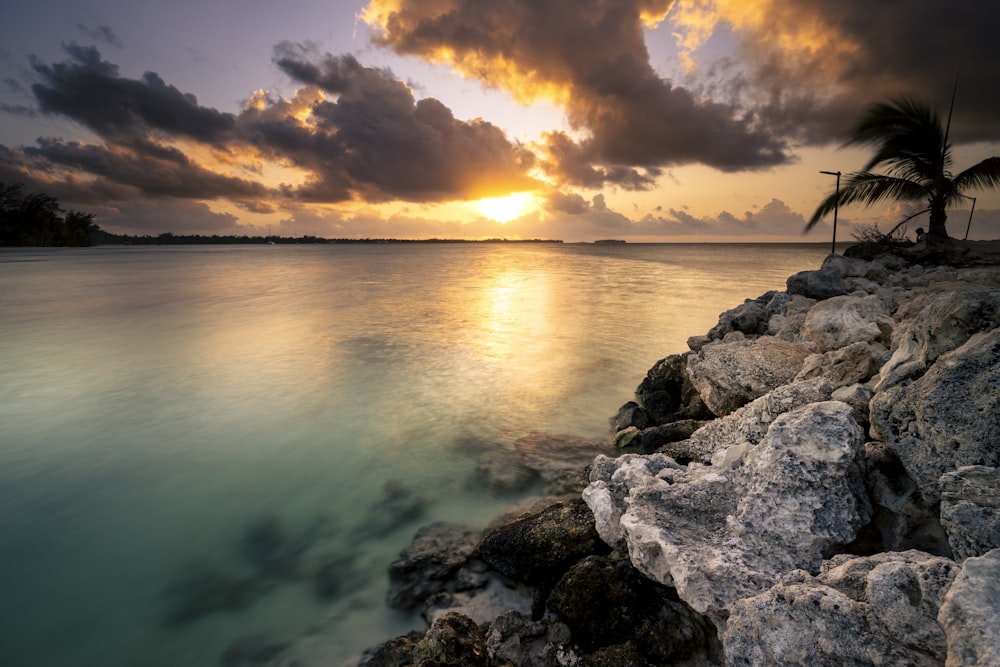 the sun is setting over the water and rocks