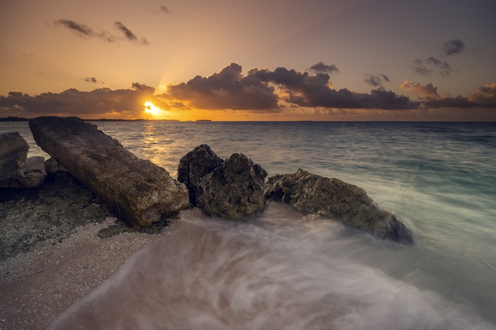 a sunset over the ocean with rocks in the foreground