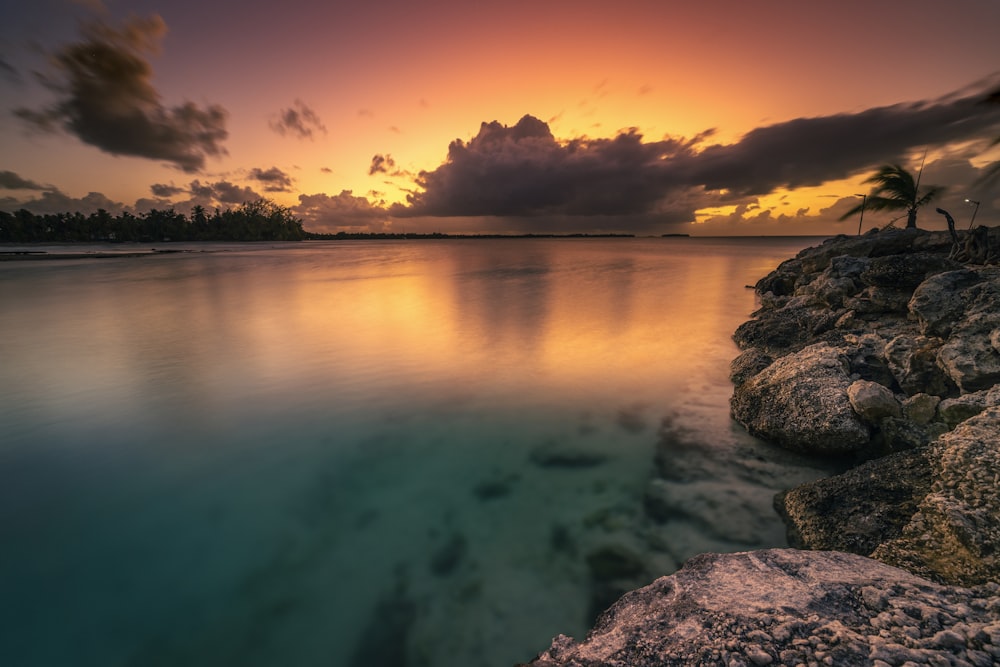 the sun is setting over the ocean with rocks in the foreground