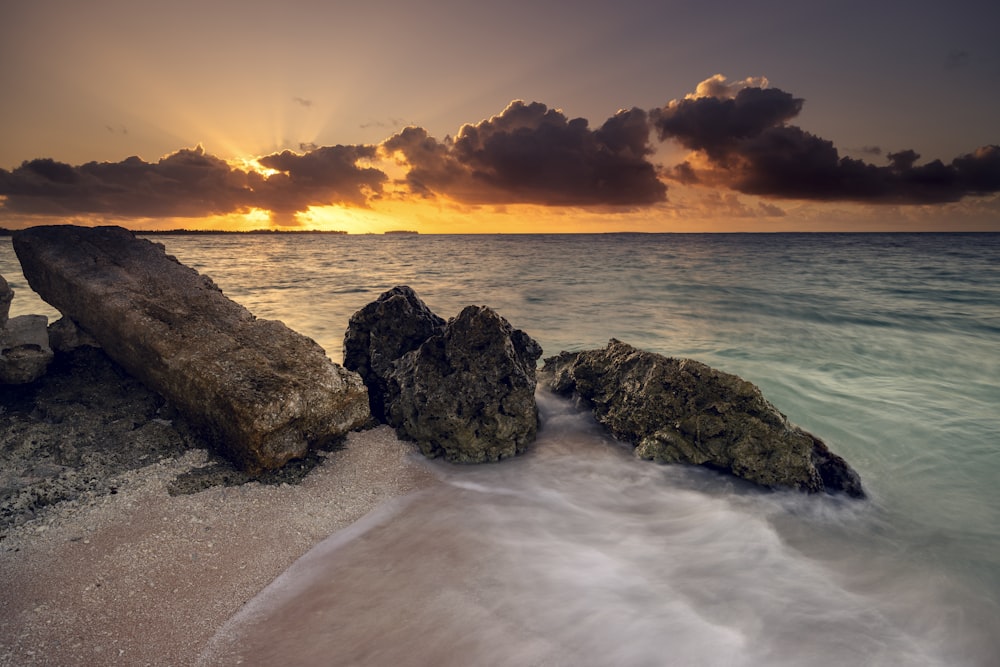 a sunset over the ocean with rocks in the foreground