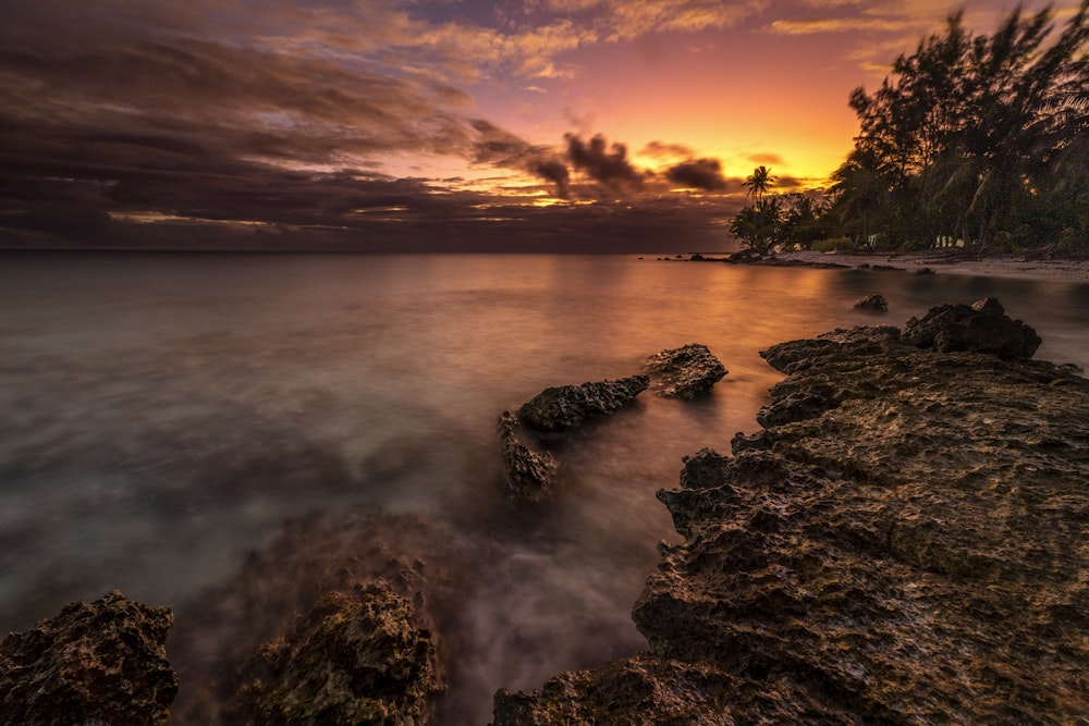 a sunset over the ocean with rocks in the foreground