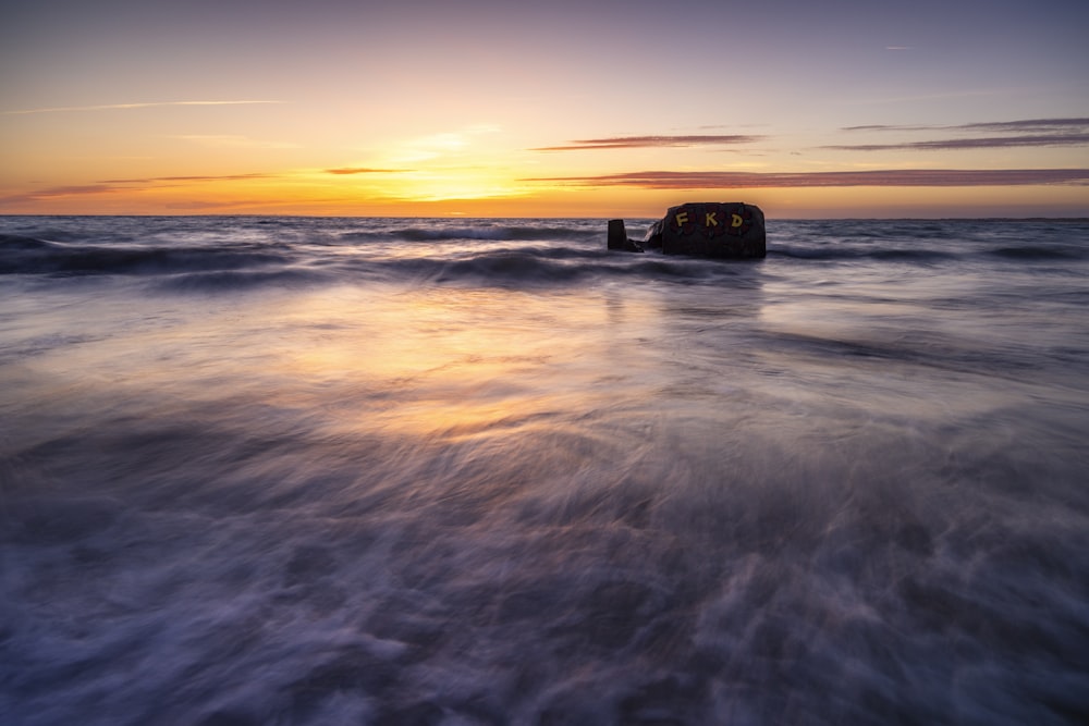 the sun is setting over the ocean with a rock sticking out of the water