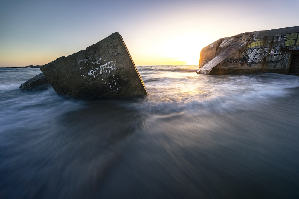 a rock in the water with graffiti on it